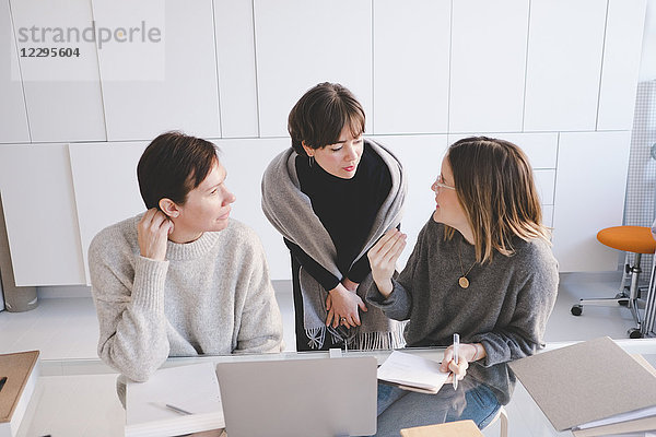 Female designer discussing with colleagues at desk in studio