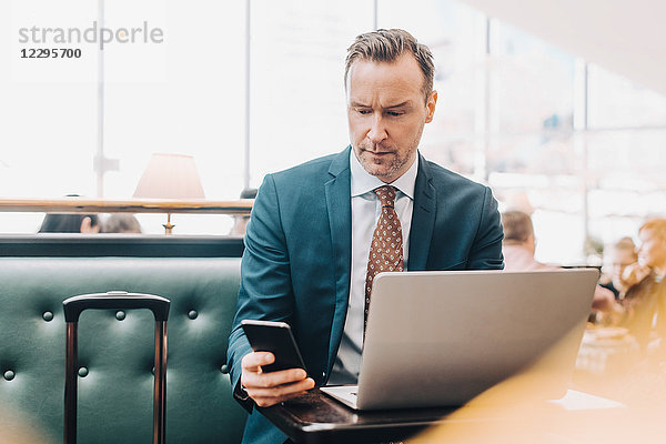 Confident mature businessman with smart phone and laptop in airport lobby