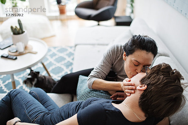 High angle view of lesbian couple kissing while sitting on sofa in living room