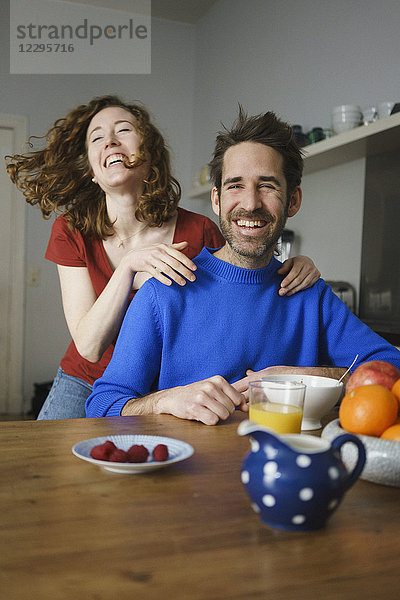 Porträt eines Mannes mit fröhlicher Frau am Tisch mit Frühstück im Zimmer