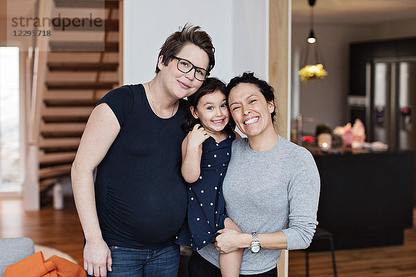 Portrait of smiling lesbian couple with daughter in living room at home