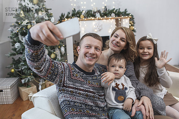 Glücklicher Mann nimmt Selfie mit Familie auf Sofa zu Hause während Weihnachten