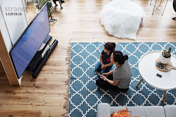 High angle view of mother and daughter watching television while sitting on floor at home