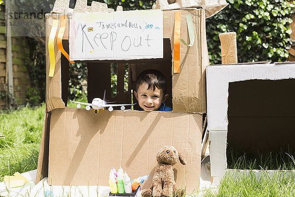 Porträt des süßen Jungen mit Spielzeug im Pappspielhaus im Hinterhof
