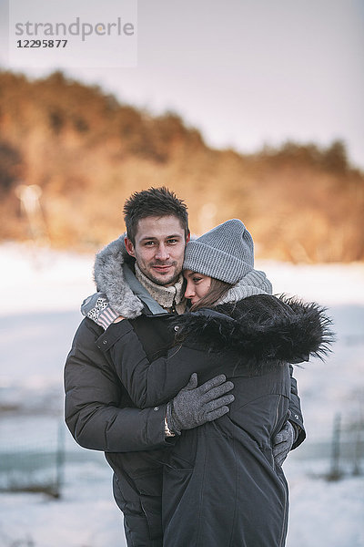 Porträt eines lächelnden Mannes  der die Frau im Winter umarmt.