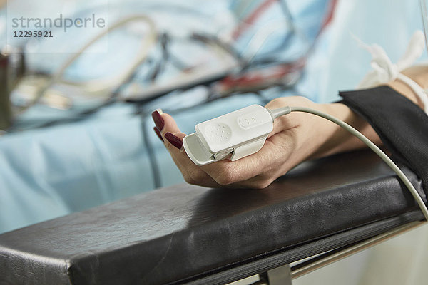Abgeschnittenes Bild eines Patienten  der ein Pulsoximeter trägt  während er im Krankenhaus auf dem Bett liegt.