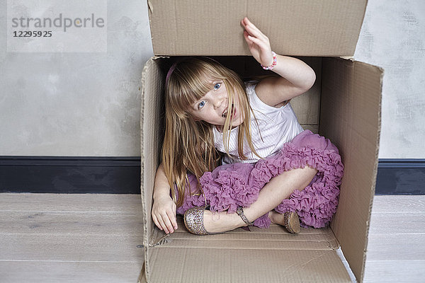 Porträt eines verspielten Mädchens im Kasten an der Wand sitzend