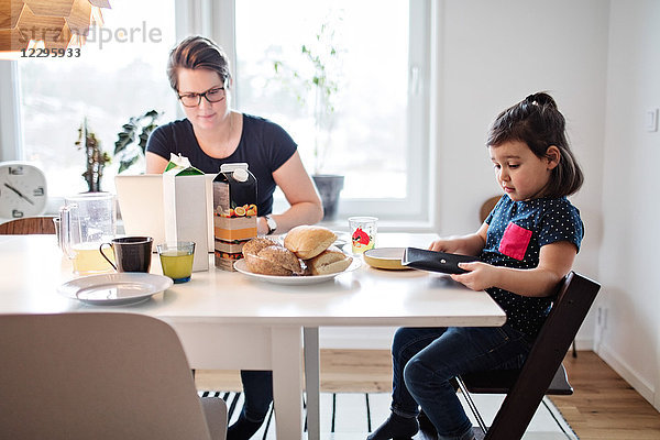 Mother using laptop while sitting with daughter during breakfast at table