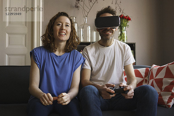 Lächelnde Frau sitzend auf einem Virtual Reality-Headset im Wohnzimmer zu Hause