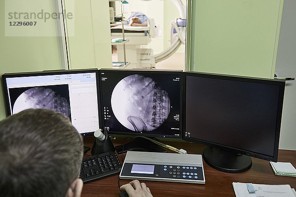 Hochwinkelansicht des Arztes beim Betrachten von medizinischen Röntgenbildern am Computer im Krankenhaus