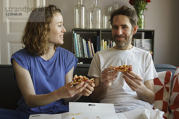 Fröhliches  erwachsenes Paar auf dem Sofa sitzend  frische Pizza im Wohnzimmer zu Hause essend.