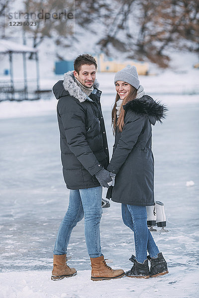 Volle Länge des glücklichen Paares  das über die Schulter schaut  während es auf der Eisbahn steht.