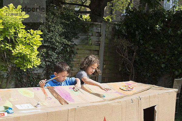 Multi-ethnische Freunde malen Pappspielhaus im Hinterhof an einem sonnigen Tag