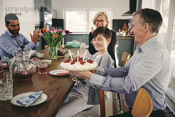 Smiling boy with grandparents and father with birthday cake at table