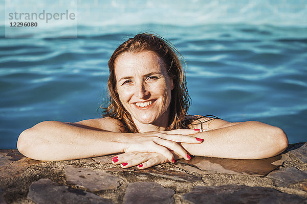 Porträt einer glücklichen Frau am Pool an einem sonnigen Tag