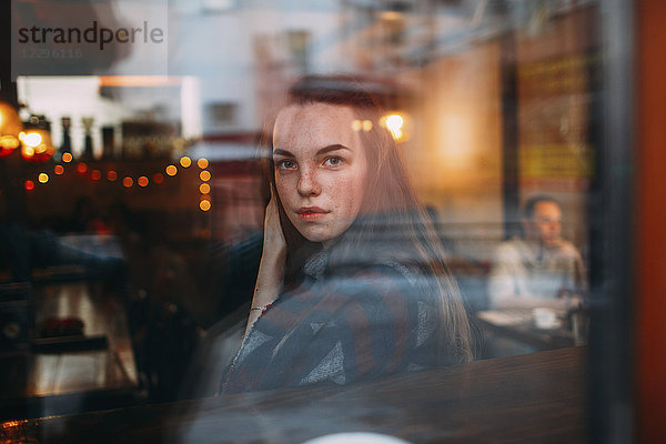 Schöne junge Frau durch das Caféfenster gesehen