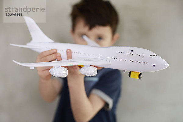 Junge spielt mit dem Modellflugzeug und steht an der grauen Wand