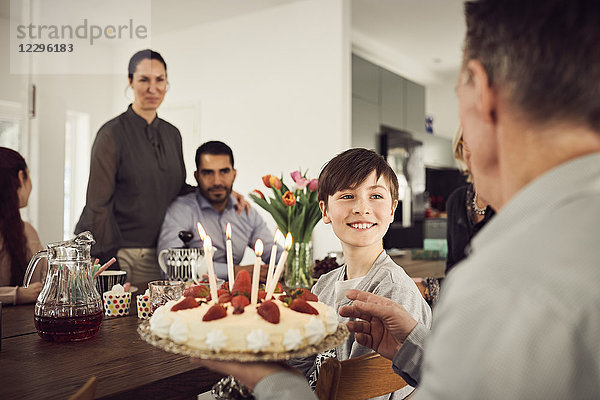 Smiling boy looking at grandfather holding birthday cake with family in party