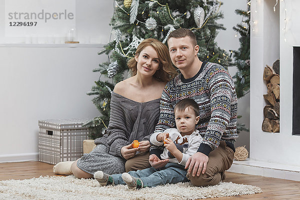 Porträt von Vater und Mutter sitzend mit Sohn auf einem Teppich am Weihnachtsbaum zu Hause