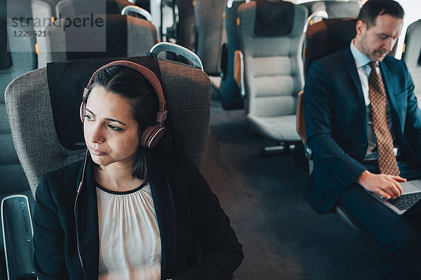 Businesswoman using headphones while traveling with businessman in train