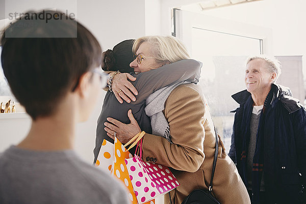 Senior woman embracing daughter while standing at doorway with family