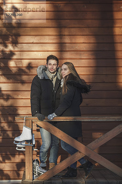Volle Länge des Paares stehend mit Schlittschuhen an der Holzwand