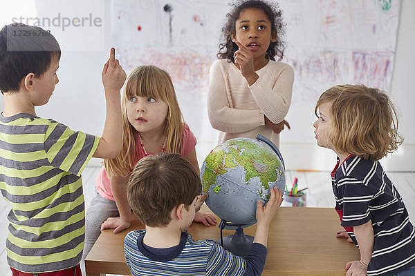 Kinder diskutieren bei der Erkundung des Globus bei Tisch in der Vorschule