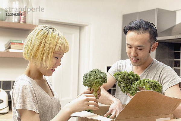 Lächelndes junges Paar  das frisches Gemüse aus dem Karton nimmt.