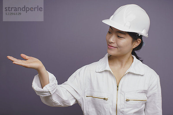 Zuversichtliche junge Bauarbeiterin mit Gesten vor violettem Hintergrund