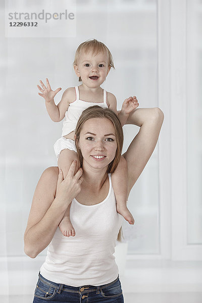 Porträt einer glücklichen Mutter  die ihre Tochter auf den Schultern trägt.