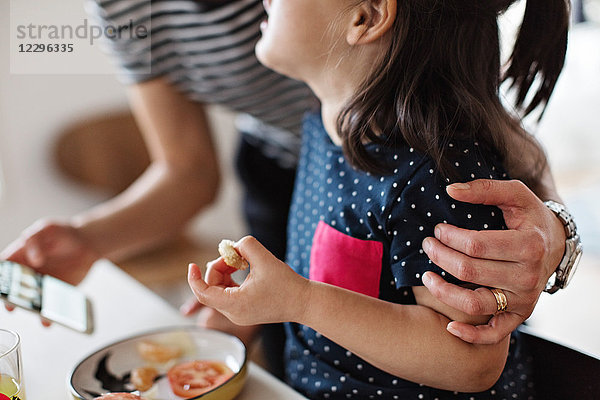 Midsection of mother embracing daughter while having breakfast at dining table