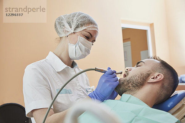 Zahnarzt mit OP-Maske und Kappe bei der Untersuchung des männlichen Patienten