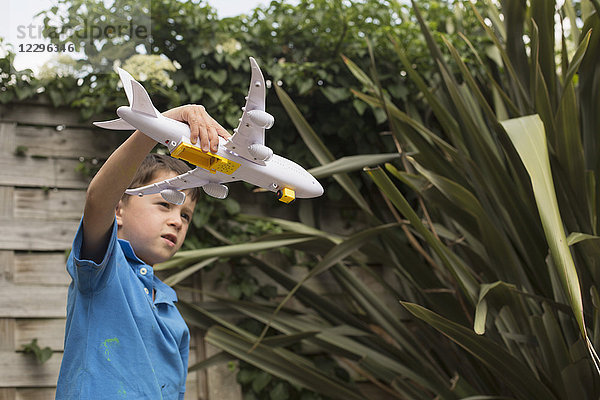 Junge spielt mit Spielzeugflugzeug gegen Pflanzen im Hinterhof