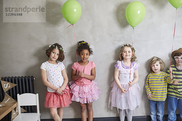 Porträt von Mädchen und Jungen mit grünen Luftballons  die an der Wand stehen