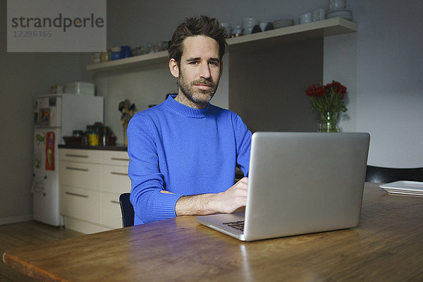 Porträt eines selbstbewussten Mannes mit Laptop am Tisch in der Küche