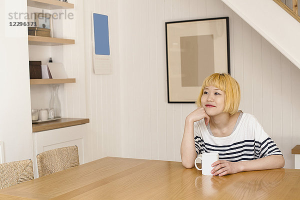 Nachdenklich lächelnde Frau beim Kaffee am Tisch an der Wand sitzend