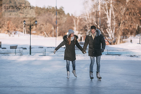 Volle Länge des glücklichen Paares  das sich an den Händen hält  während es auf der Eisbahn Schlittschuh läuft