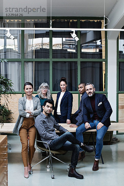 Full length portrait of confident business team at table in creative office