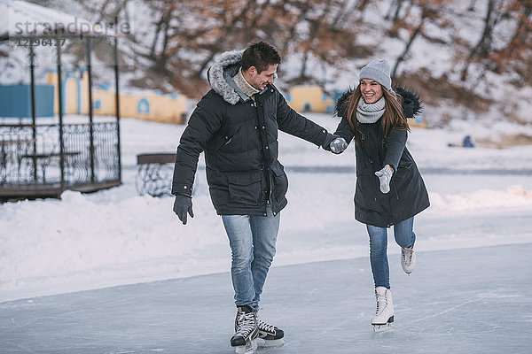 Volle Länge des glücklichen Paares  das beim Eislaufen Händchen hält.