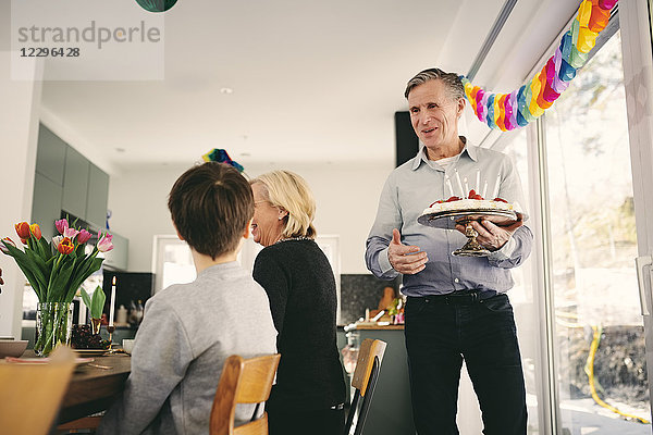 Boy looking at grandfather holding birthday cake in party