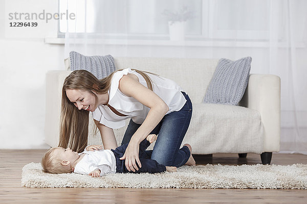 Verspielte Mutter und Tochter auf dem Teppich zu Hause