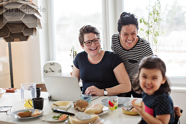 Cheerful mothers looking at daughter having breakfast on dining table