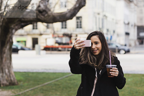 Glückliche Frau fotografiert vom Smartphone aus  während sie in der Stadt einen Drink hält.