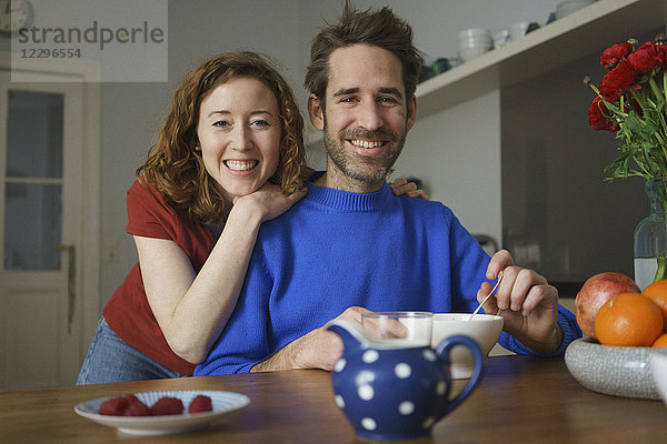 Porträt des lächelnden mittleren Erwachsenenpaares bei Tisch mit Frühstück im Zimmer