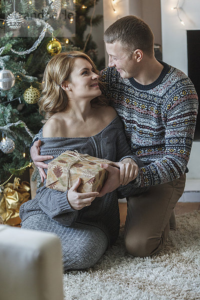 Glückliches Paar mit Geschenk vom Weihnachtsbaum zu Hause