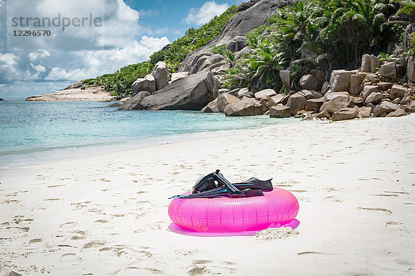 Tauchflossen mit Tauchermaske auf rosa aufblasbarem Ring am Strand gegen bewölkten Himmel  Seychellen