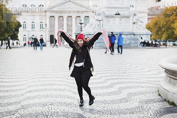 Porträt einer fröhlichen Frau  die auf dem Stadtplatz gegen den Bau in der Stadt tanzt  Lissabon  Portugal