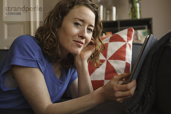 Porträt einer selbstbewussten Frau mit digitalem Tablett auf dem Sofa zu Hause