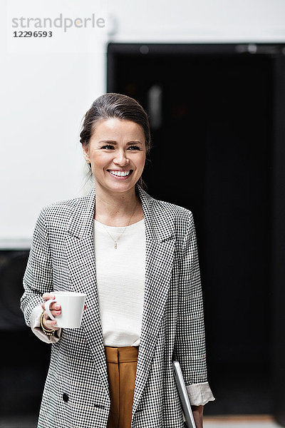 Portrait of smiling businesswoman looking away while holding coffee cup at office