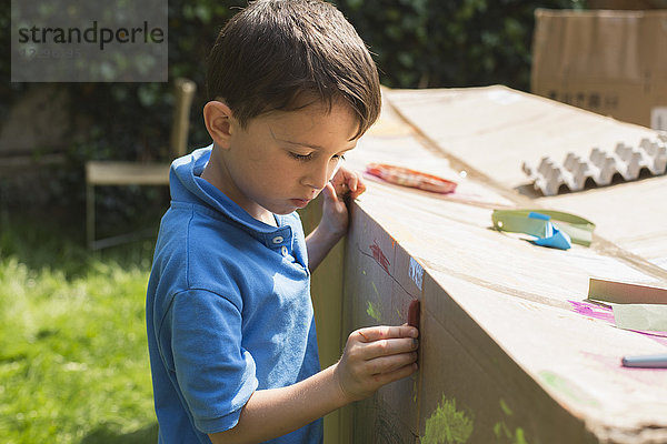 Jungenmalerei auf Pappspielhaus im Hinterhof bei Sonnenschein